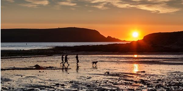 A family walk with their dog along Daymer Bay as the sun sets